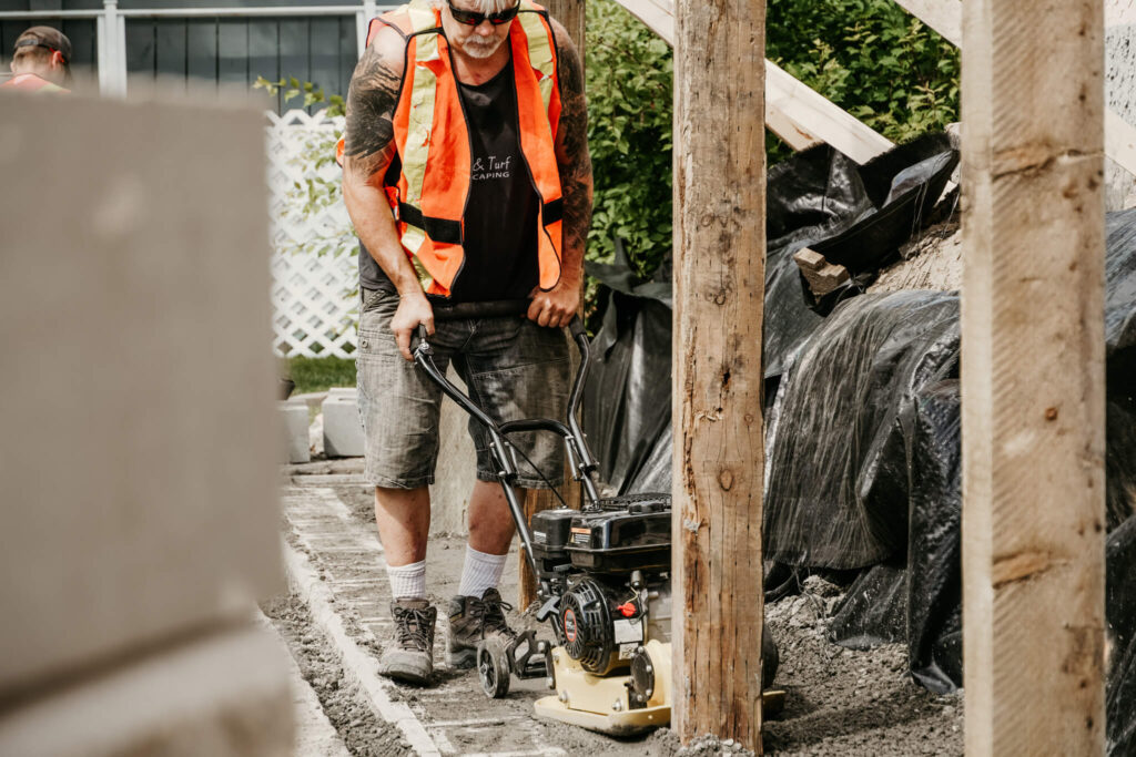 An Earth and Turf Landscaping Edmonton worker pushing a piece of retaining wall -related machinery near a wooden post.