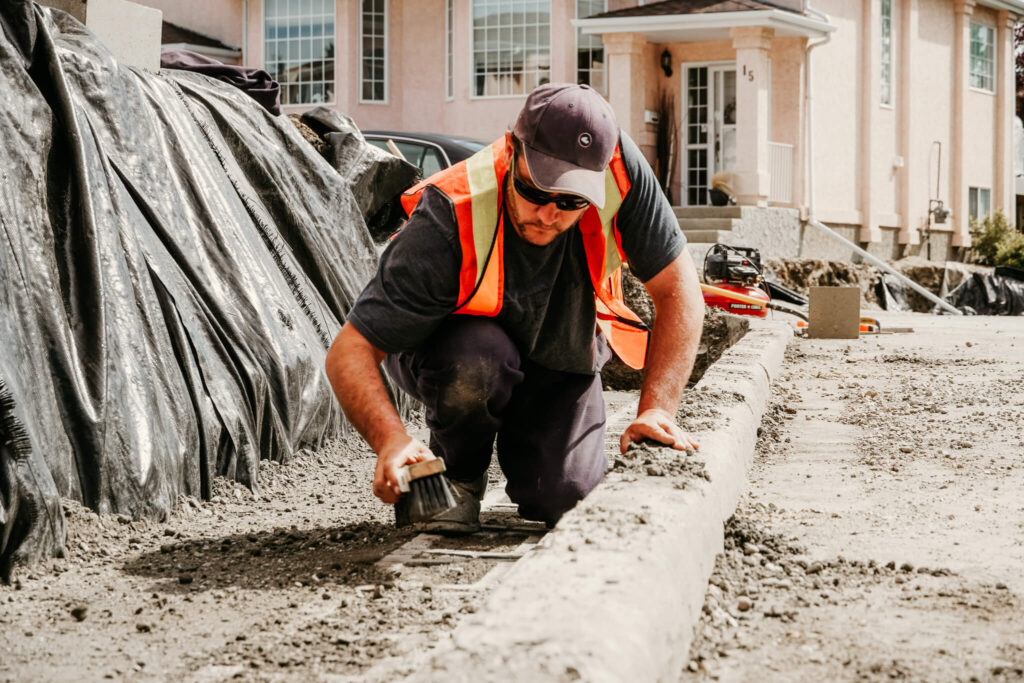 A worker brushing away dirt on an Earth and Turf Landscaping Edmonton retaining wall job site.