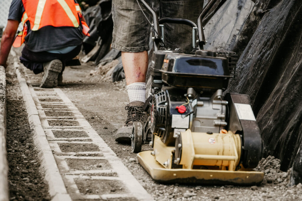 An Earth and Turf Landscaping Edmonton worker operating a piece of machinery while another worker does detailing on a retaining wall.