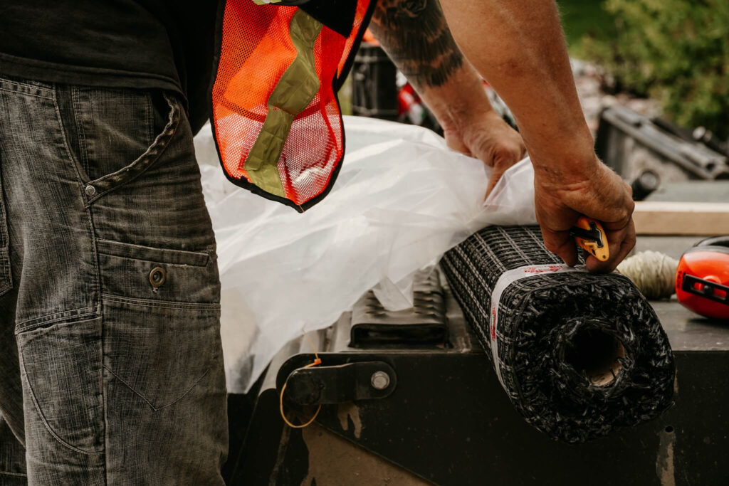 Close-up of an Earth and Turf Landscaping Edmonton worker unpacking a roll of wire mesh on a retaining wall job site.