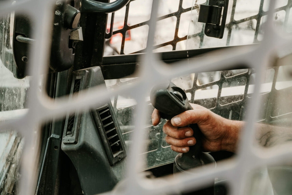 Close-up of an Earth and Turf Landscaping Edmonton worker operating a digger joystick on a retaining wall job site.