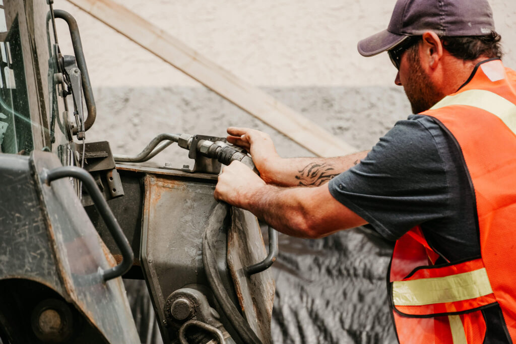 An Earth and Turf Landscaping Edmonton worker securing a piece of machinery on a retaining wall job site.