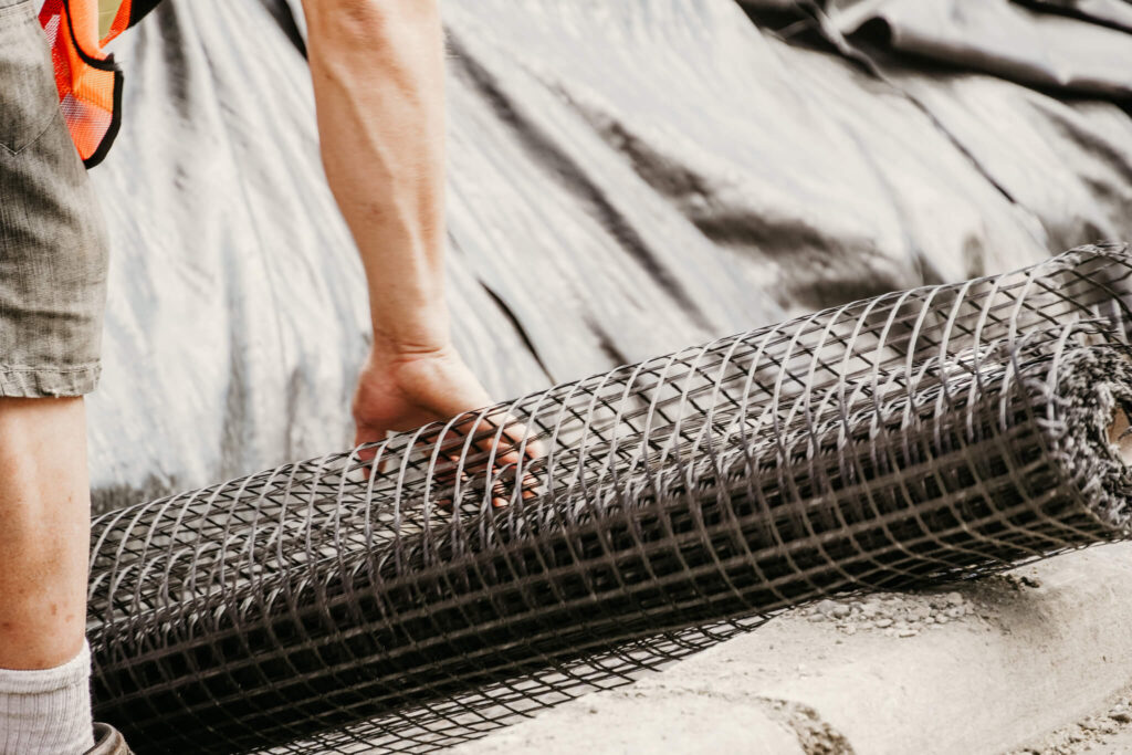 Close-up of an Earth and Turf Landscaping Edmonton worker rolling out wire mesh on a retaining wall job site.