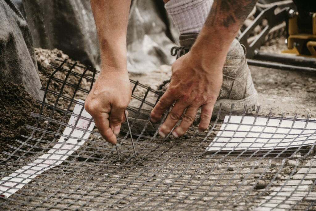 Close-up of an Earth and Turf Landscaping Edmonton working placing a peg in wire mesh on a retaining wall job site.