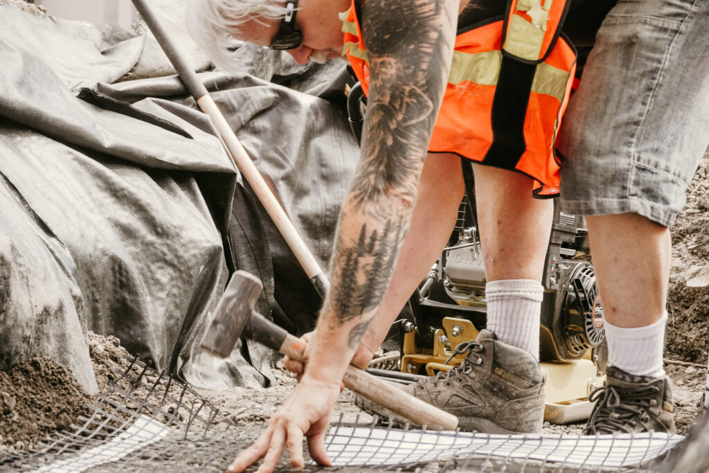 An Earth and Turf Landscaping Edmonton worker hammering a peg down into wire mesh on a retaining wall project.