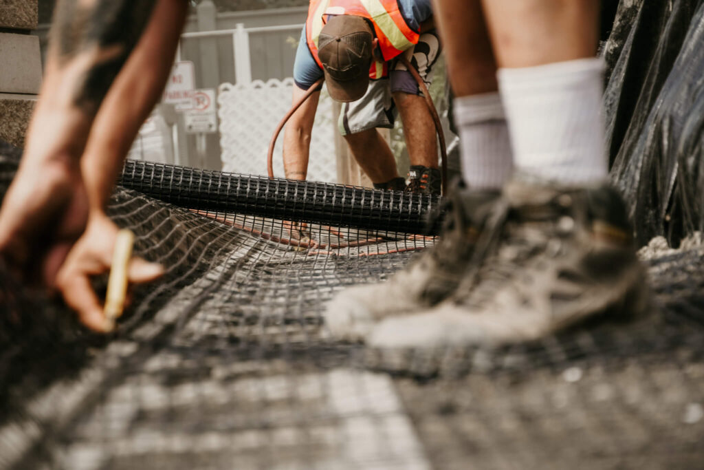 Two workers laying and trimming wire mesh on an Earth and Turf Landscaping Edmonton retaining wall job site.