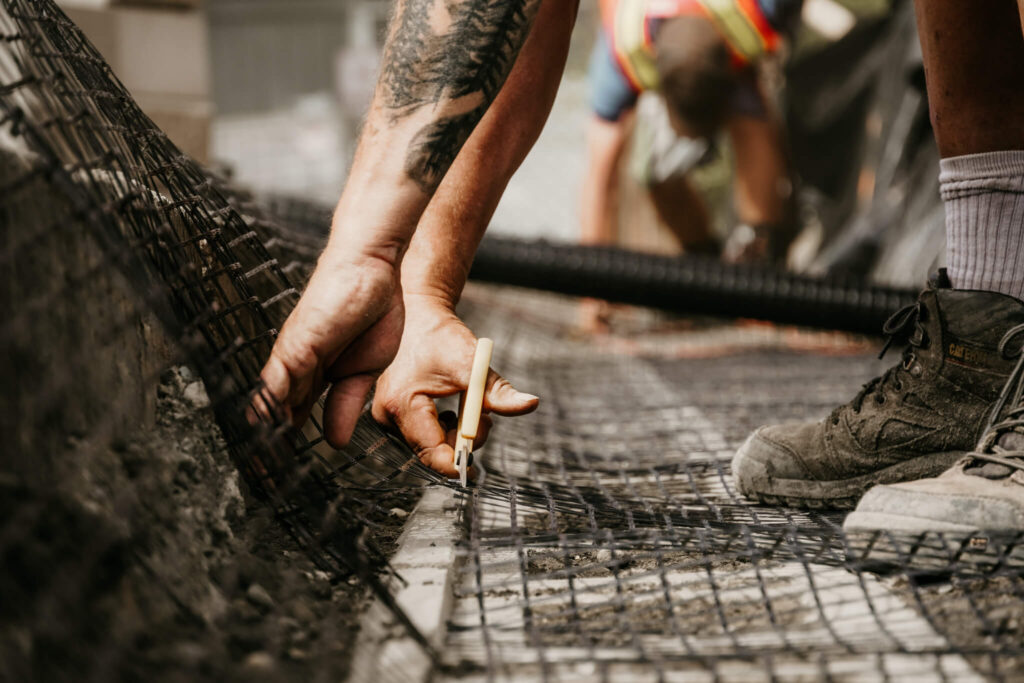 Close-up of an Earth and Turf Landscaping Edmonton worker trimming wire mesh on a retaining wall job site.