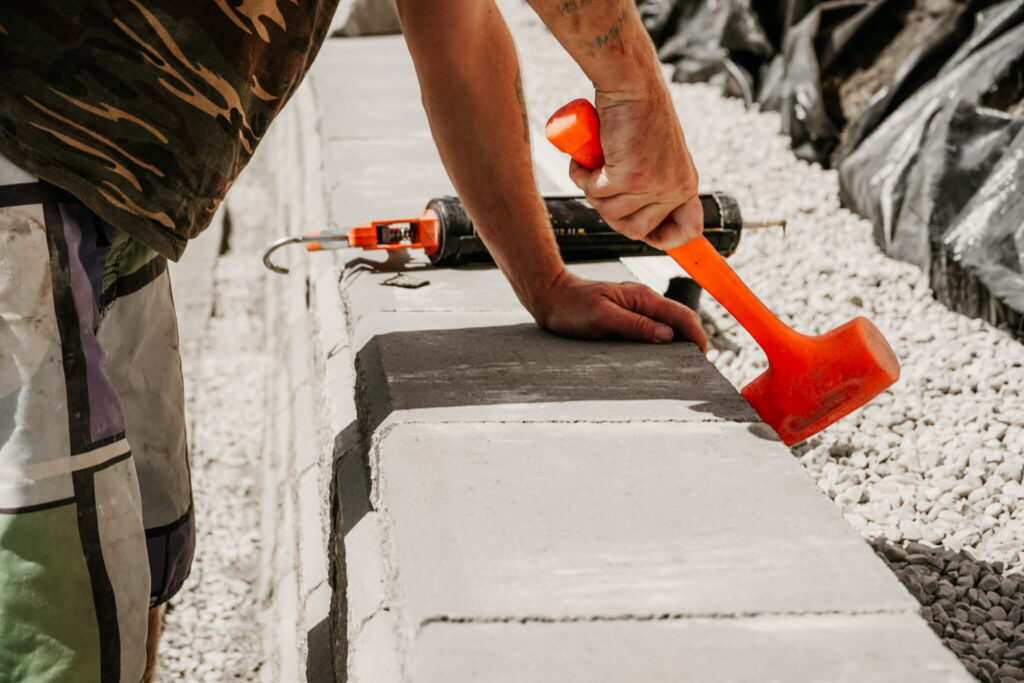 Side view of an Earth and Turf Landscaping Edmonton worker using a mallet on a retaining wall.