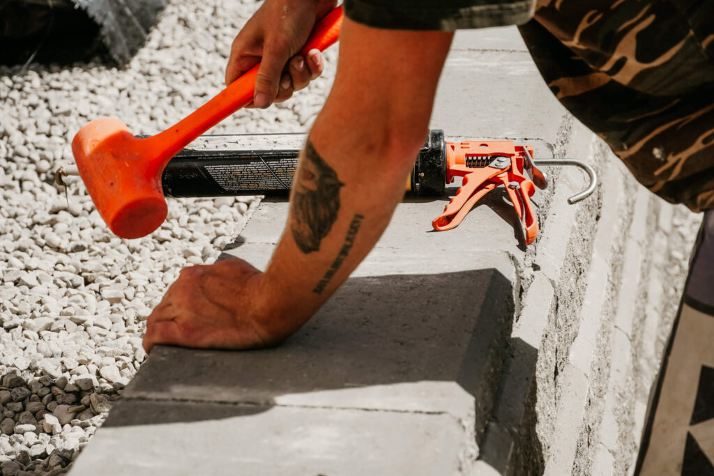 Close-up of an Earth and Turf Landscaping Edmonton worker using a mallet on a retaining wall.