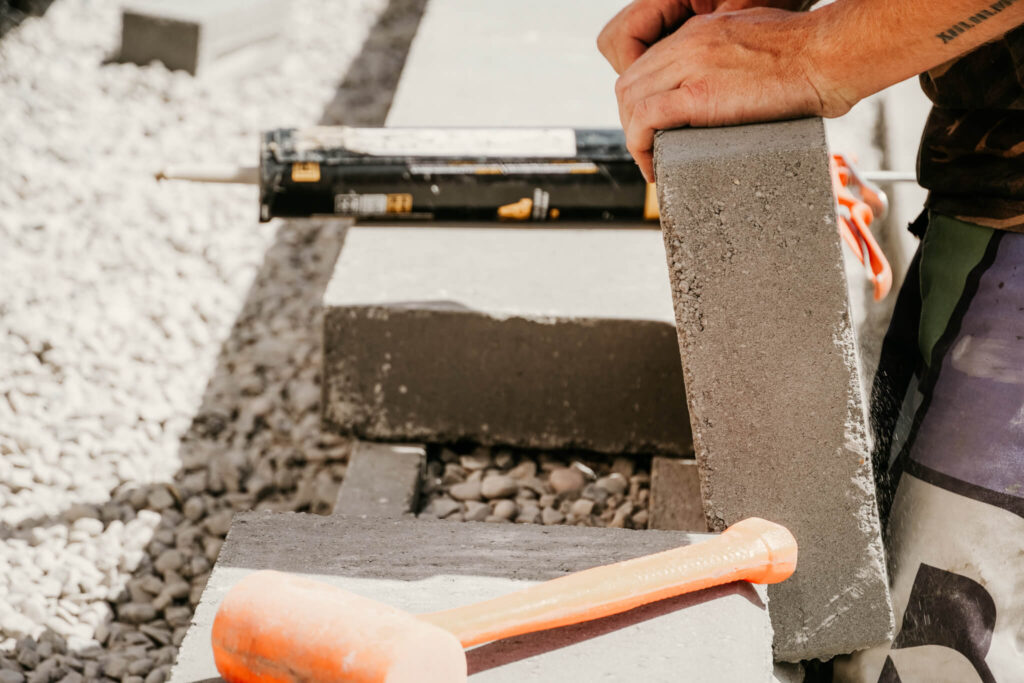 Close-up of an Earth and Turf Landscaping Edmonton worker laying a brick on a retaining wall.