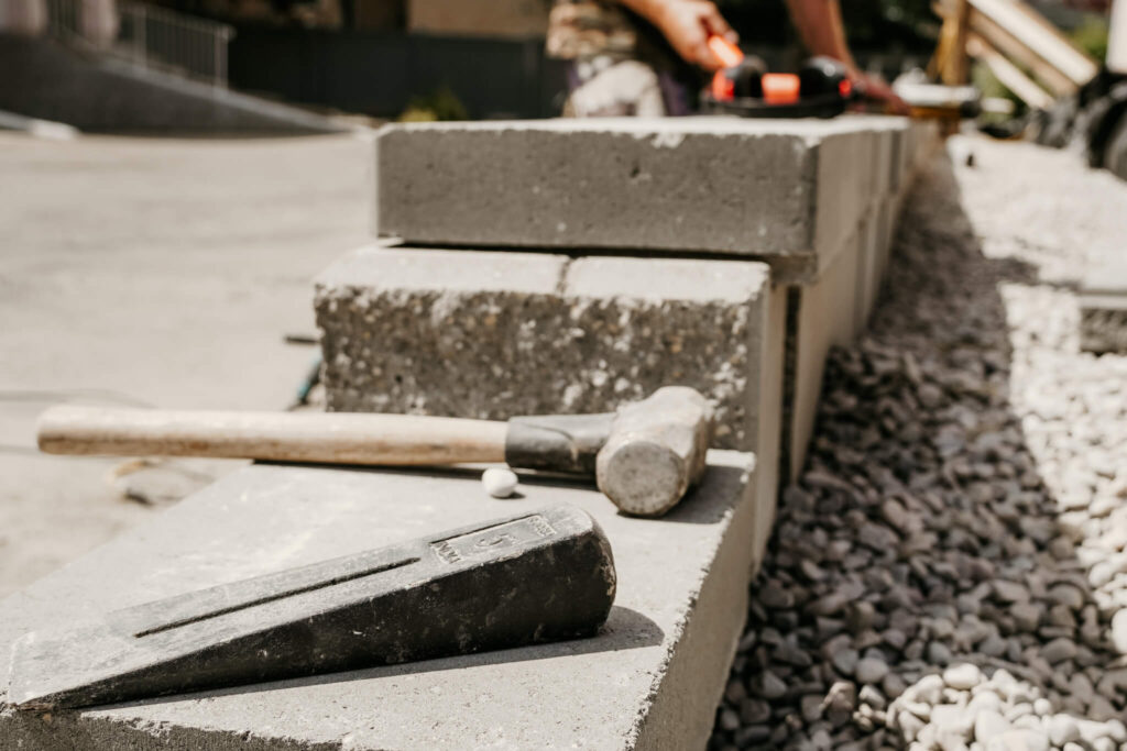 Close-up of a hammer and chisel sitting on top of an Earth and Turf Landscaping Edmonton retaining wall.