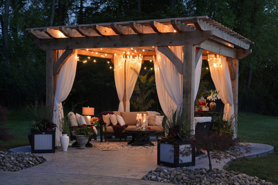 Cushioned furniture and potted plants are warmly lit under a wooden terrace in summer.