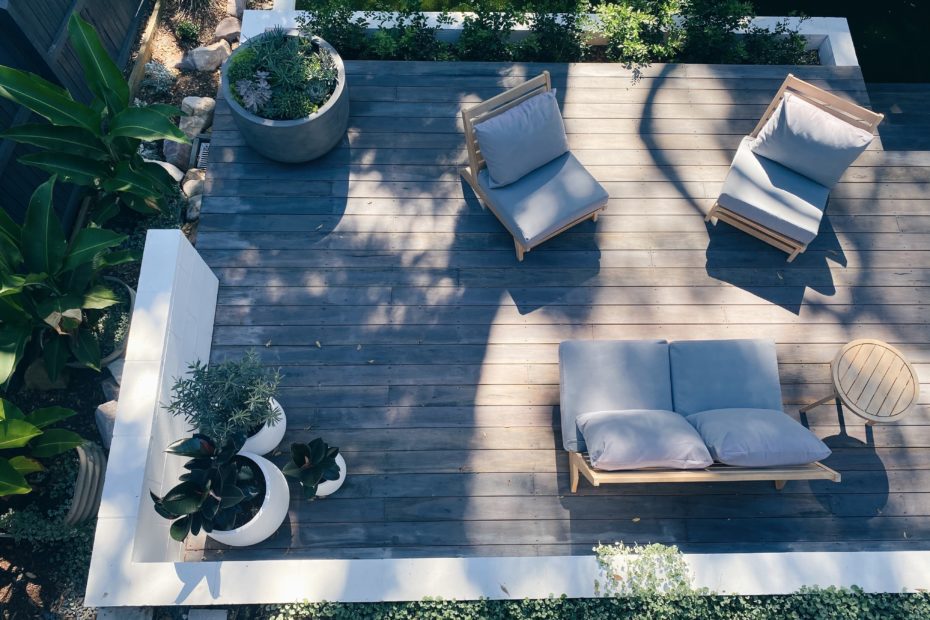 Cushioned patio furniture and potted plants sit on a modern wooden patio.